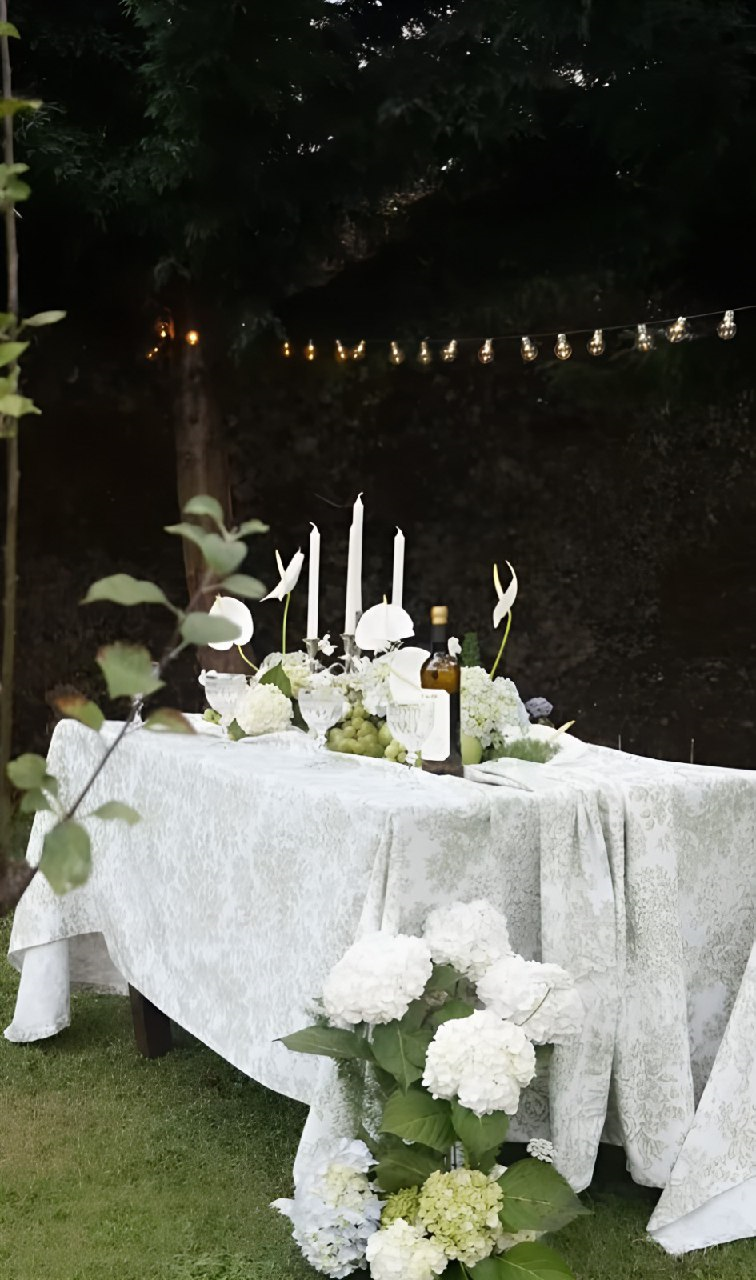 Mesa con flores blancas, velas y cristalería preparada en el jardín de Santa Emilia