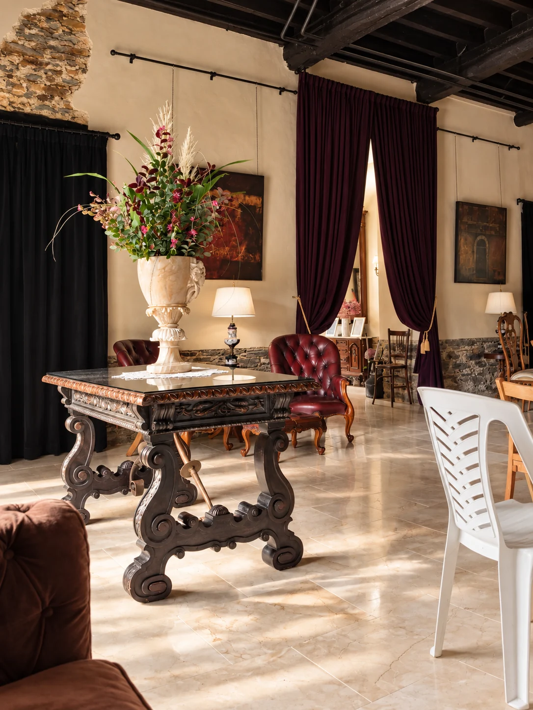 Mesa tallada, urna floral y cortinas granates del salón